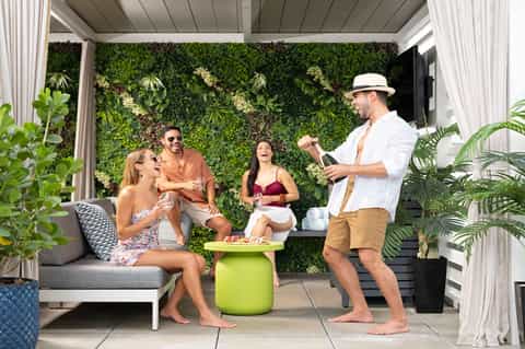 Outdoor lounge area with grey seating, living plant wall backdrop, green accent table, and four people socializing under pergola