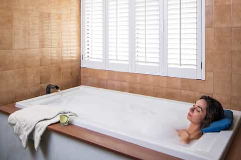 Woman relaxing in soaking tub with window view and rolled towel nearby