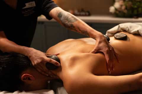 Professional massage therapist performing stone massage treatment on client's back