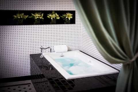 Modern spa bathroom with white bathtub, white tile walls, and decorative yellow lilies display