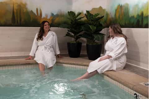 Spa hot tub with two women in white robes and potted plants indoors