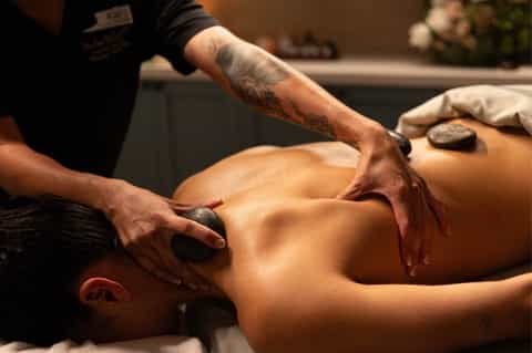 Massage therapist performing hot stone treatment on client's back in spa setting