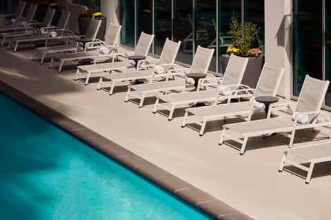 Row of white lounge chairs lined along resort pool deck near glass building