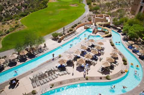 Aerial view of resort pool with turquoise water, loungers, and umbrellas adjacent to golf course