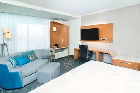Contemporary hotel room with bed, sofa seating, wooden desk, TV, and modern furnishings