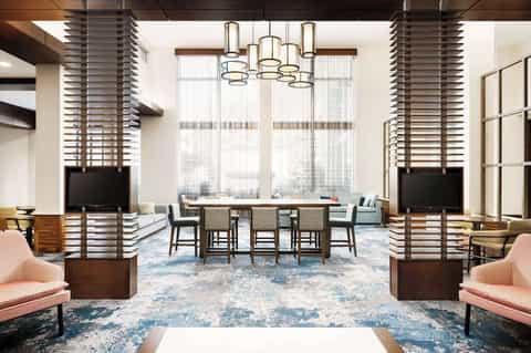 Modern hotel lobby lounge with high ceilings, pendant lighting, seating areas, and floor-to-ceiling windows