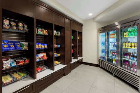 Hotel convenience store with dark wood snack shelves on left and refrigerated beverage cases on right