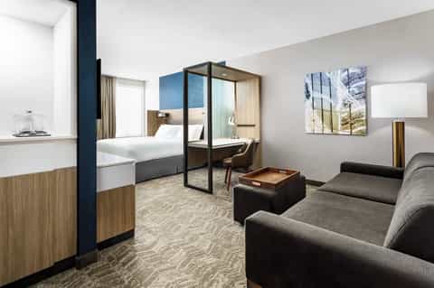 Modern hotel suite with four-poster bed, sitting area, wood accents, and contemporary design