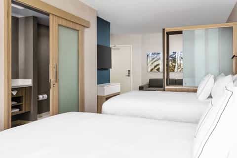 Modern hotel bedroom with two queen beds, wooden furnishings, and large mirror wall