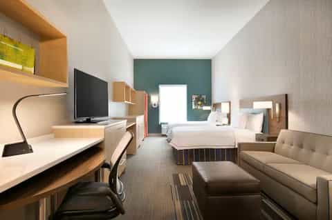 Modern hotel room with two beds, work desk, TV, teal accent wall, and contemporary furnishings