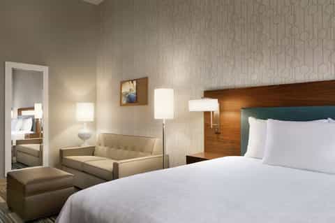 Modern hotel room with queen bed, sofa, wood headboard, and neutral décor