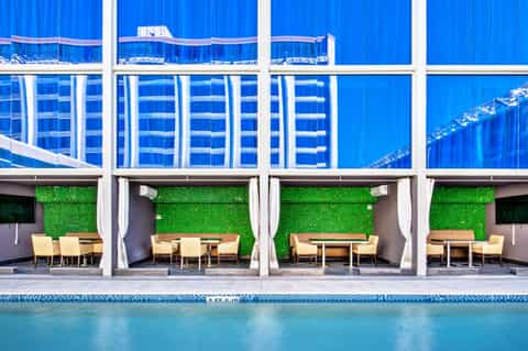 Resort poolside with blue cabanas, green living walls, yellow lounge chairs, and modern white pergola structures