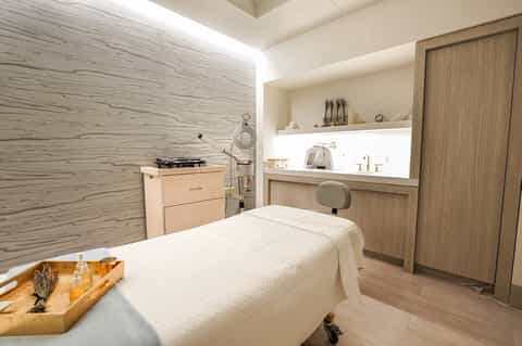 Modern spa treatment room with neutral wood and stone finishes, massage table, and wellness amenities