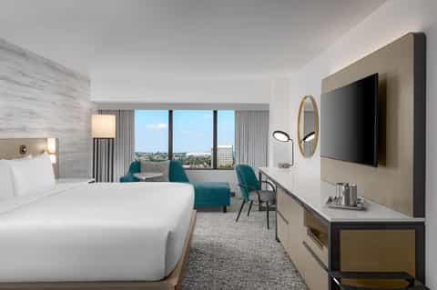 Modern hotel room with king bed, teal seating, and city skyline view