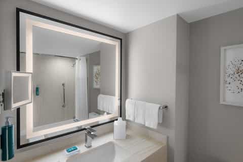Modern bathroom with illuminated mirror, walk-in shower, and marble finishes