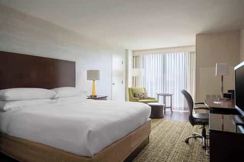Contemporary hotel room with queen bed, green accent chair, and balcony access