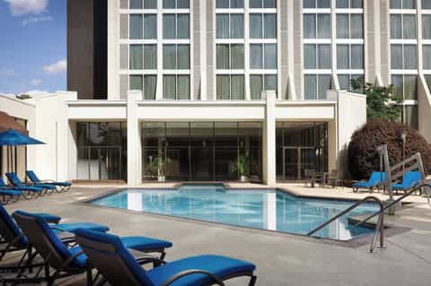 Hotel courtyard pool with rectangular design, blue lounge chairs, modern white facade building with grid windows, and manicured landscaping