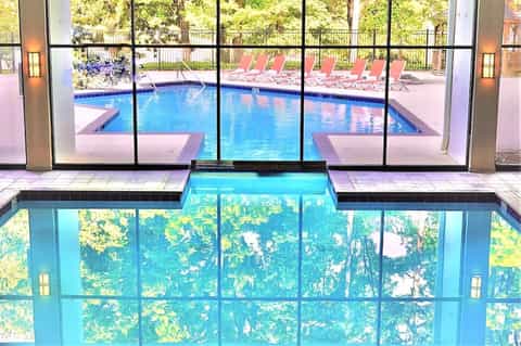 Indoor pool overlooking outdoor pool area with pink lounge chairs and forest views