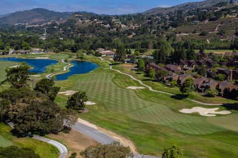 Aerial view of championship golf course with blue water hazards and hillside residential community