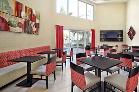 Hotel lounge with red patterned seating, black tables, palm views, and modern décor