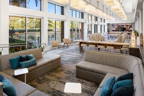 Bright modern resort lounge with neutral sofas, floor-to-ceiling windows, outdoor deck, fireplace, and contemporary furnishings
