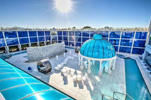 Modern rooftop pool area with turquoise dome structure, white lounge seating, and blue glass windscreens under bright sun