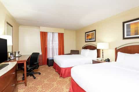 Traditional hotel room with two queen beds, red accents, desk area, and warm yellow walls
