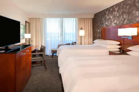 Hotel bedroom with two beds, wood furnishings, ocean view balcony, and flat-screen TV