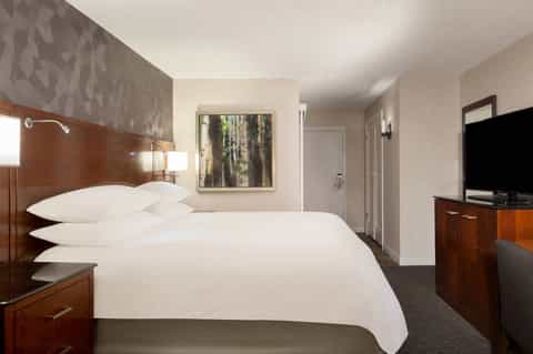 Hotel bedroom with queen bed, wood headboard, flat-screen TV, and neutral décor
