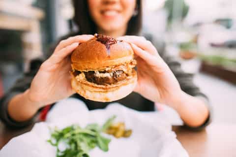 Woman holding gourmet burger with caramelized onions outdoors