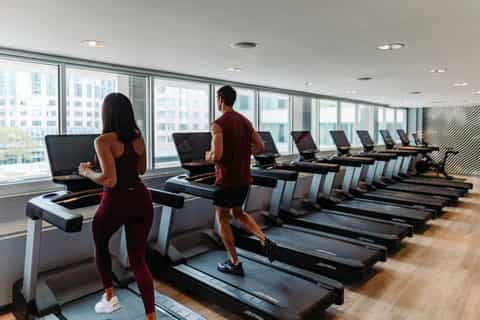 Modern fitness center with rows of treadmills, floor-to-ceiling windows overlooking city buildings