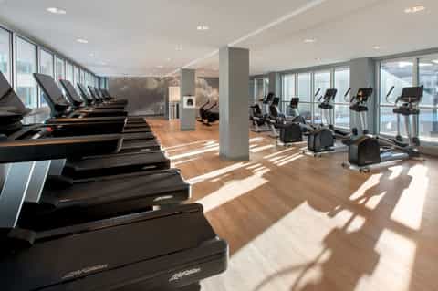 High-rise gym with treadmills, exercise bikes, wooden floors, and floor-to-ceiling windows