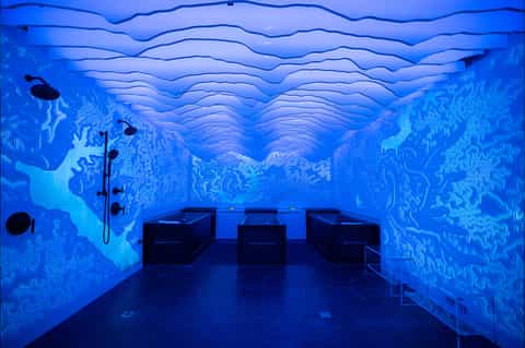Underwater-themed spa room with blue wave wall murals and black lounge chairs for relaxation