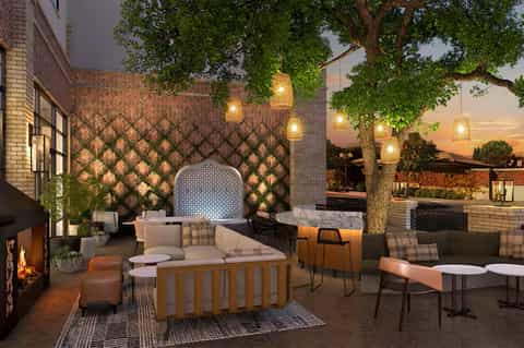 Evening patio with herringbone brick wall, fire pit, hanging lights, loungers, and dining area