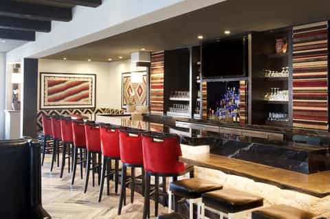 Premium lounge with red bar stools, full bar, Native American art, and TV display