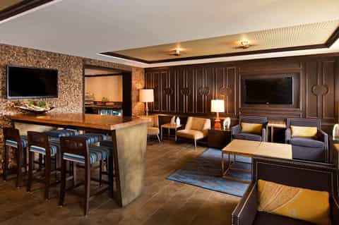 Upscale lounge and bar with wood paneling, fireplace, leather seating, and modern televisions