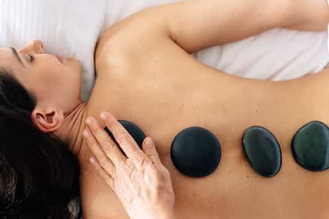Spa massage treatment with heated black stones applied to client's back