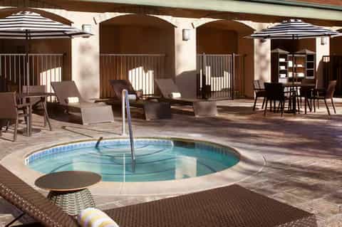 Resort spa courtyard with circular hot tub, arched covered structures, umbrellas, loungers, and architectural columns