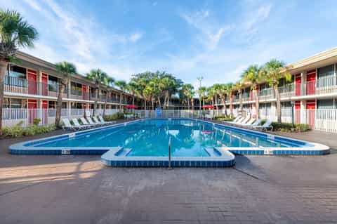 Resort pool with red and white building courtyard, palm trees, and lounge chairs