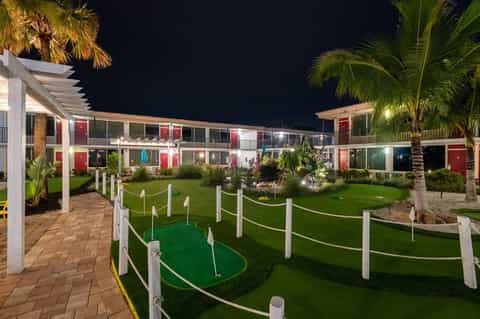 Night view of resort courtyard with illuminated buildings, mini golf course, palm trees, and manicured lawn