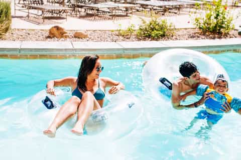 Family enjoying resort pool with inflatable floats, woman and man with child in turquoise water