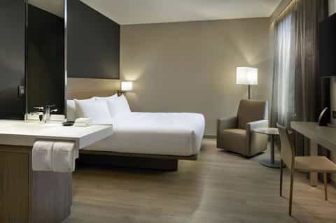 Contemporary hotel room with king bed, white linens, modern desk, and minimalist neutral decor