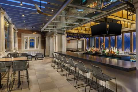 Modern rooftop bar with glass ceiling, bar seating, and city night views