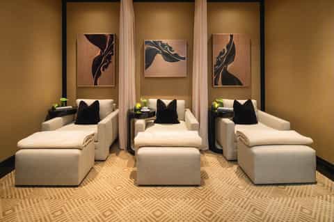 Spa relaxation room with three cream chaise lounges, gold walls, and framed abstract artwork