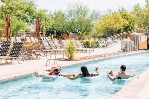 Guests relaxing in resort pool with lounge chairs and umbrellas in background