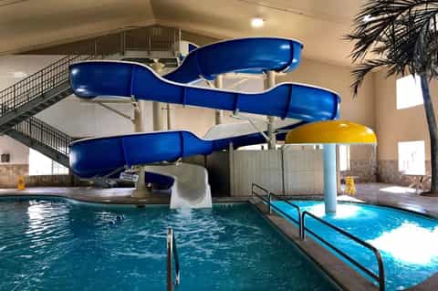 Indoor water park with blue twisting slides, pool, and palm trees in bright atrium space