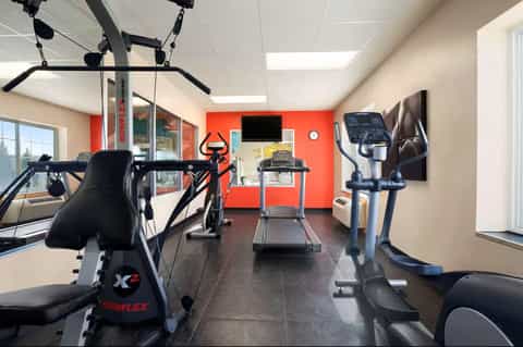 Compact fitness room with stationary bike, treadmill, and exercise equipment against red wall