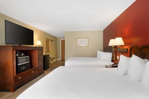 Hotel guest room with two queen beds, fireplace with TV, warm color scheme, and wood furnishings
