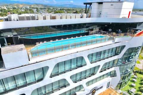 Modern high-rise hotel with rooftop turquoise pool, glass balconies, mountain views, and contemporary architecture