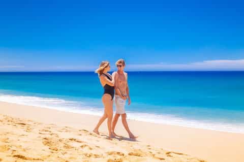 Couple standing together on a pristine sandy beach with turquoise ocean water and clear sky